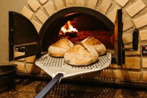 Three sourdough loaves bake in a rustic brick oven, showcasing traditional culinary craftsmanship.